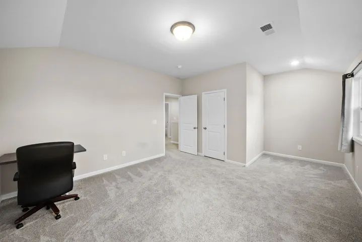 A spacious, naturally illuminated room featuring vaulted ceilings and plush carpeting, perfect for flexible living arrangements.