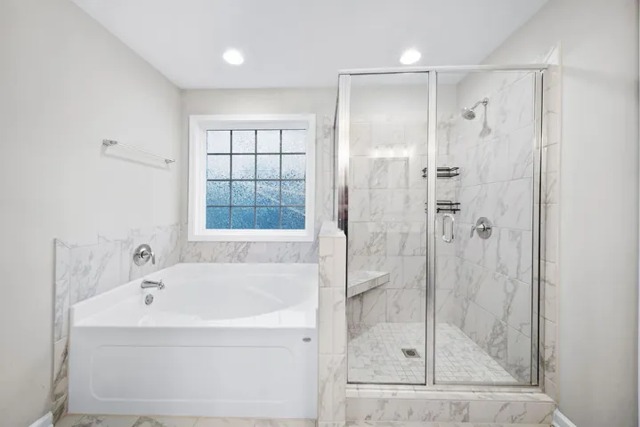 Sleek, marbled tile and a deep soaking tub define this pristine bathing area.