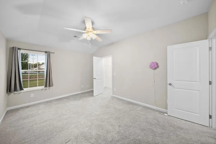 A quiet bedroom with vaulted ceilings, a window providing natural illumination, and plush carpet.