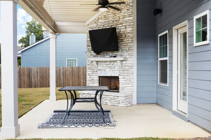 An inviting outdoor patio features a cozy fireplace and a ceiling fan, perfect for relaxed evenings.