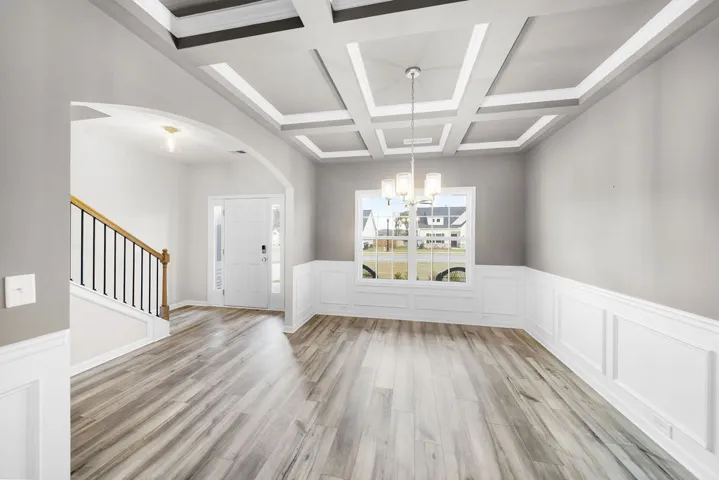 Artfully coffered ceilings crown this versatile space, featuring wainscoting and natural light streaming through the windows.