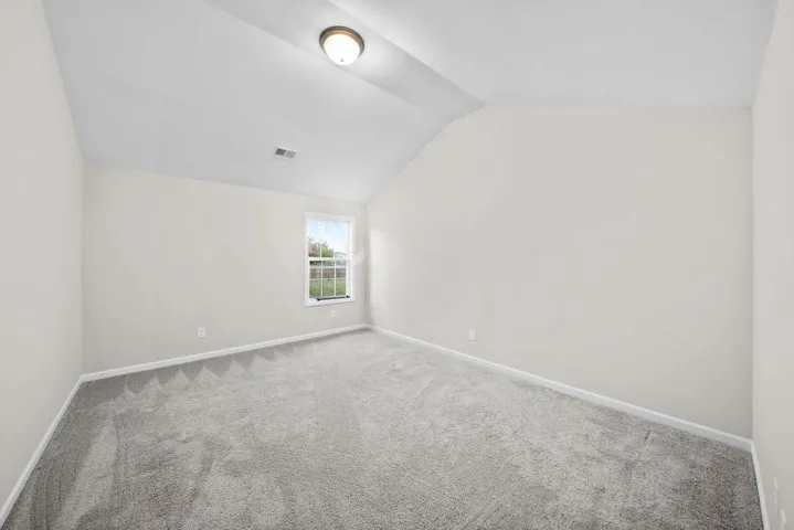 A spacious secondary bedroom features a vaulted ceiling and soft, newly installed carpeting.