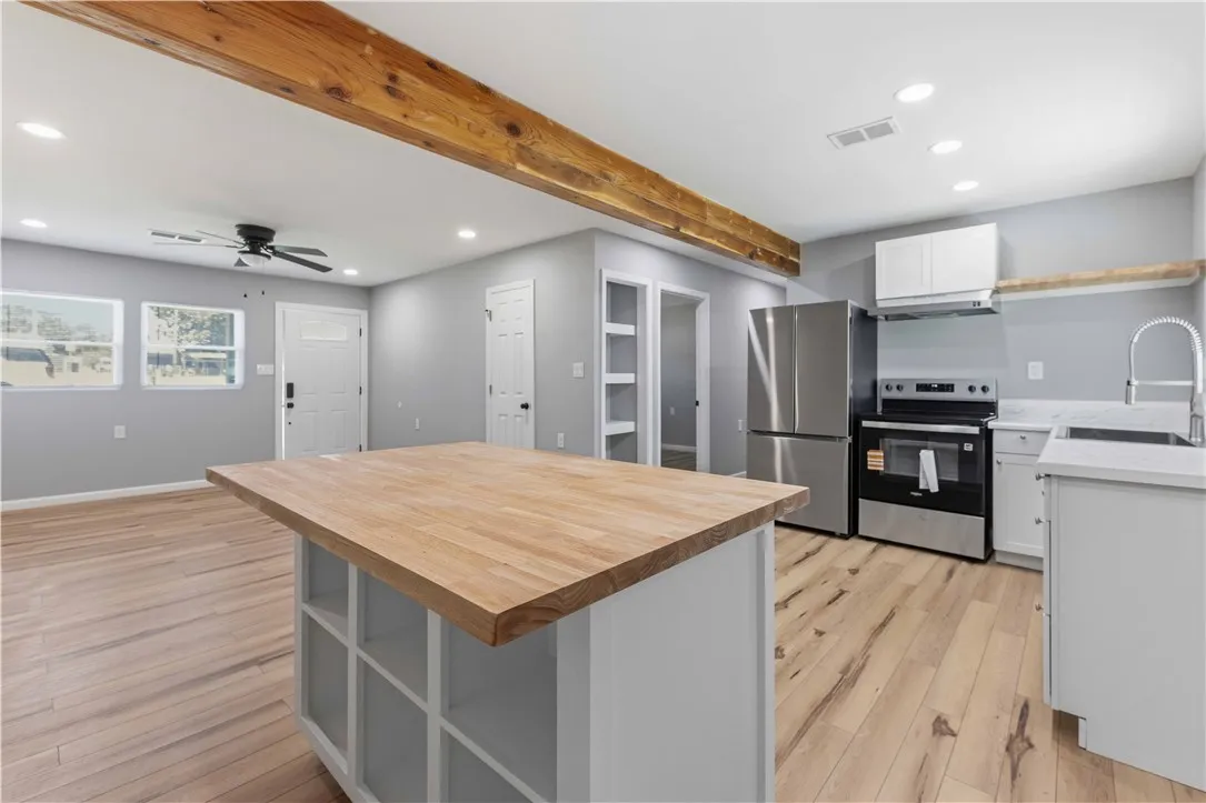 A well-lit kitchen showcasing a spacious island, rich wooden beam, and stainless steel appliances.