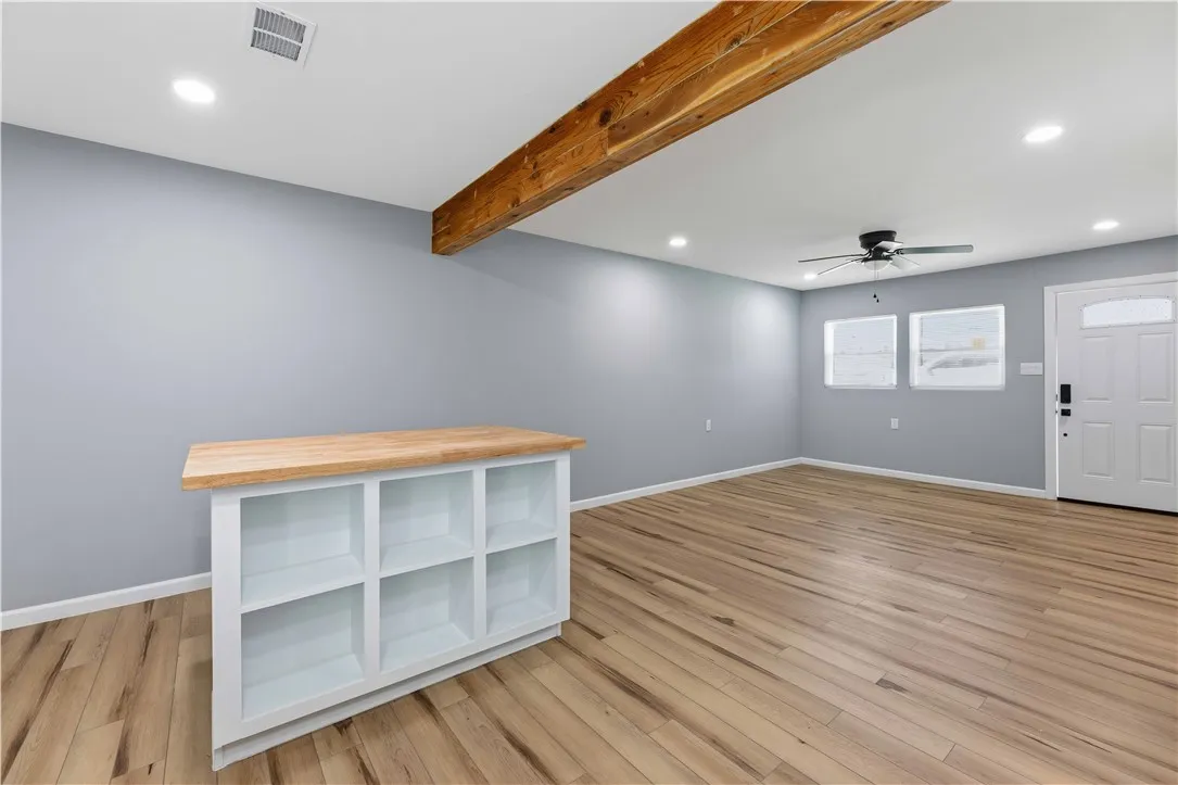 A spacious room features exposed beam accents and durable wood flooring.