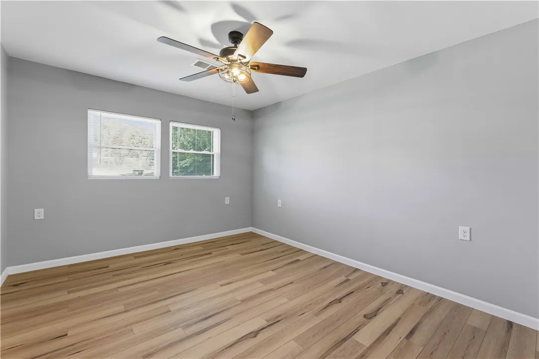 Well-lit room featuring durable wood flooring and an integrated ceiling fan.