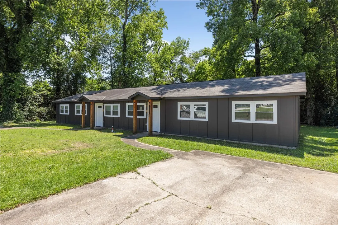 A well-maintained duplex featuring a dark gray exterior and bright white trim amidst a verdant landscape.