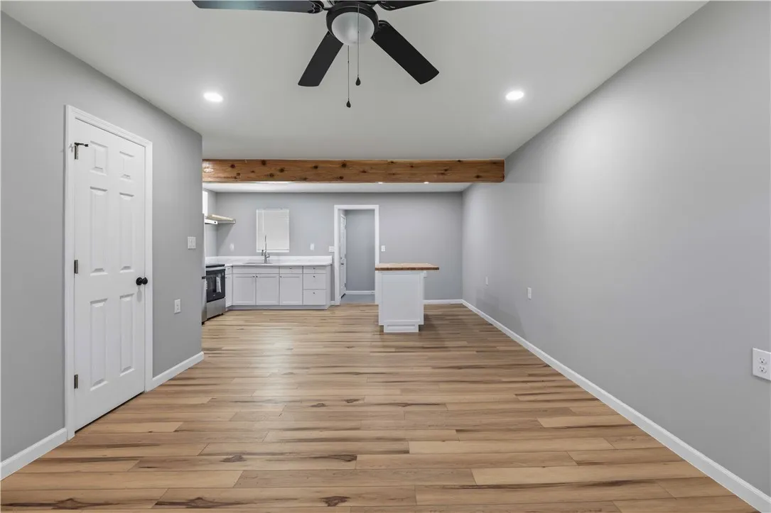 A streamlined open-concept space features warm wood flooring, an exposed beam, and a sleek kitchen with a central island.