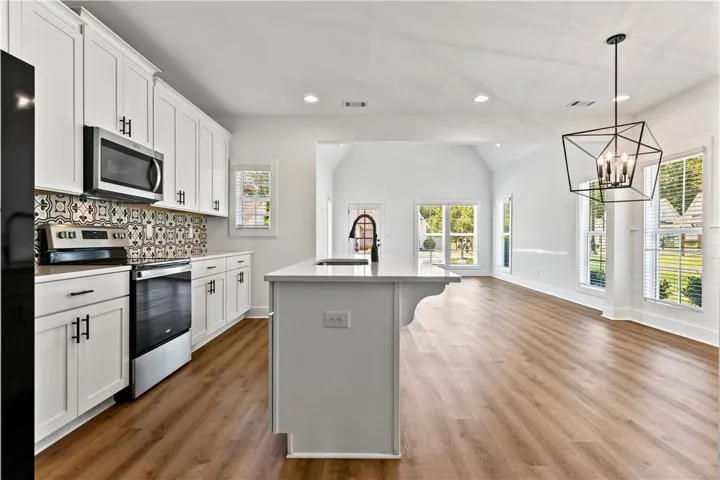 A contemporary kitchen features an island with a sink, white cabinetry, and modern appliances, all set against a backdrop of durable flooring.
