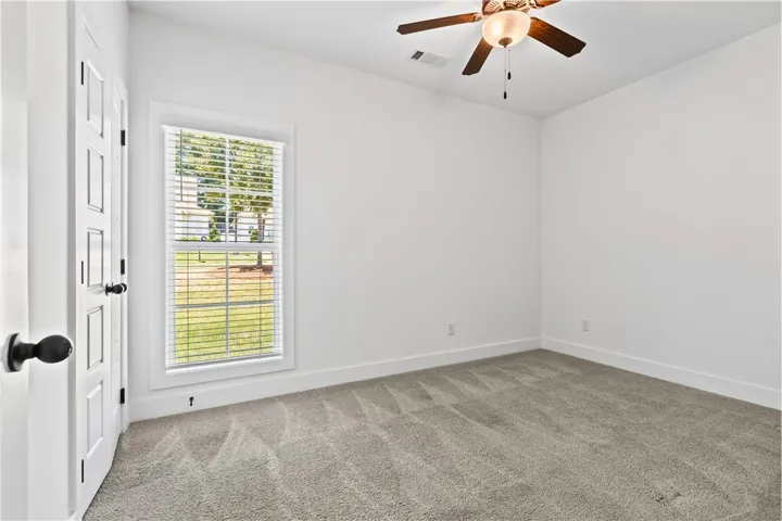 A well-lit bedroom with fresh gray carpet and a view of green landscape through the window.