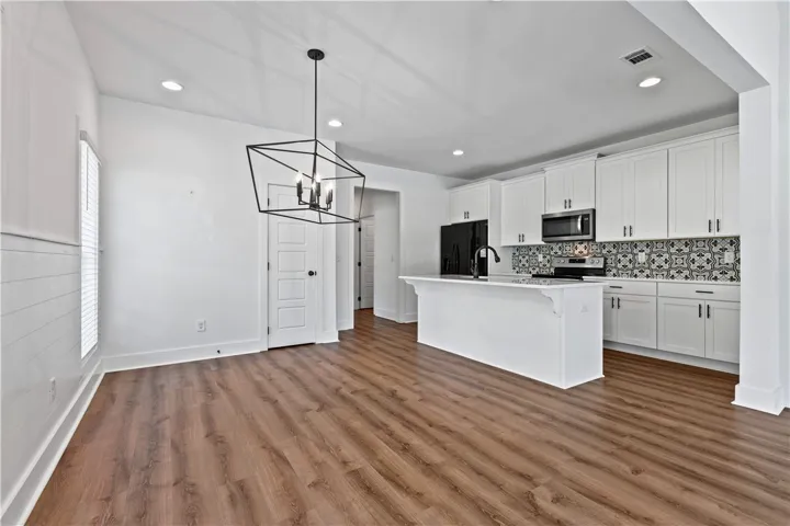 A sleek geometric chandelier illuminates the open-concept kitchen and dining area with rich hardwood flooring.