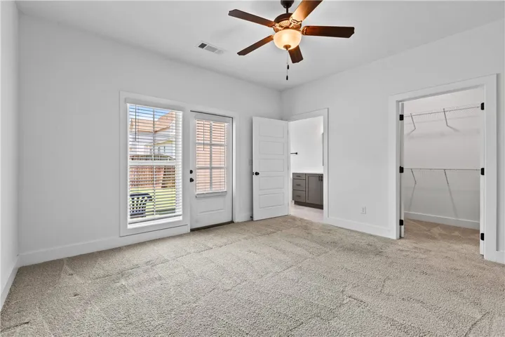 A well-lit bedroom features plush carpeting, a modern ceiling fan, and direct outdoor access.