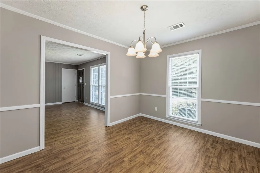 A graceful chandelier illuminates the spacious dining room, featuring rich hardwood-style flooring and natural light.