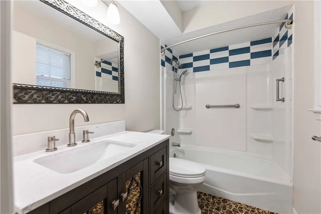 A well-appointed bath features a tiled floor, a vanity with a white countertop, and a shower with a decorative tile pattern.