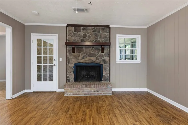 A spacious room features rich wood flooring, a striking stone fireplace with a rustic mantel, and a glass-paned door.