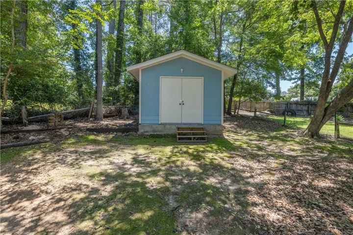 A quaint blue shed provides practical outdoor storage in a wooded backyard setting.