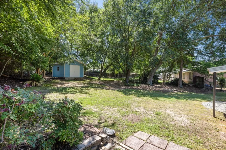 A spacious, verdant yard awaits, complete with a charming blue shed and mature shade trees.