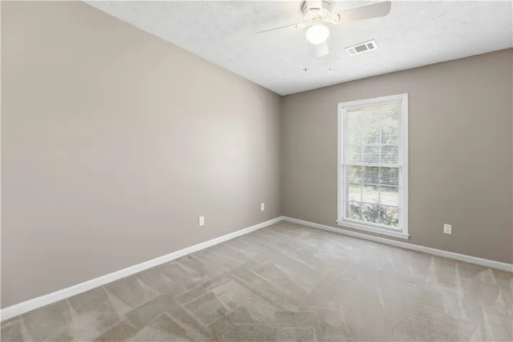 Well-lit room featuring soft carpet, a window with outdoor views, and a ceiling fan.