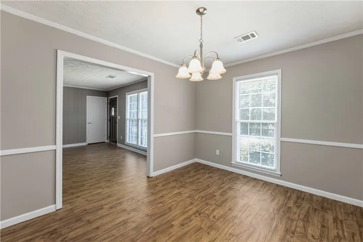 A graceful chandelier illuminates the spacious dining room, featuring rich hardwood-style flooring and natural light.