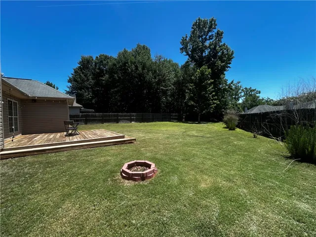 A spacious yard with a wooden deck and a charming brick fire pit beckons for outdoor enjoyment.