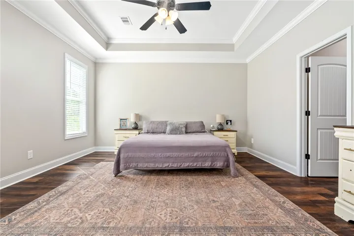 Elegant tray ceilings crown this inviting bedroom, featuring rich hardwood flooring.