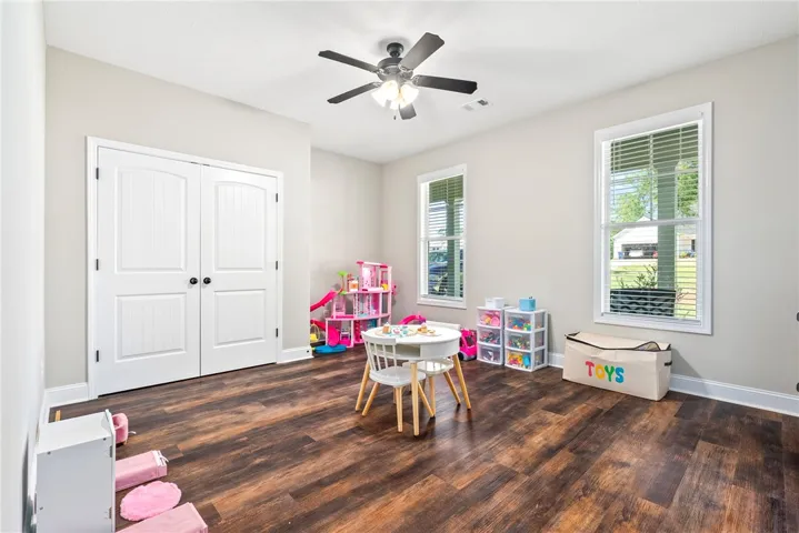 Rich hardwood-style flooring extends through this naturally illuminated bedroom with a modern ceiling fan.