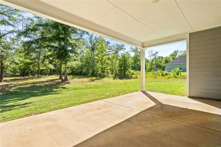 A spacious covered patio provides a serene outlook onto a verdant, expansive yard bordered by a natural tree line.
