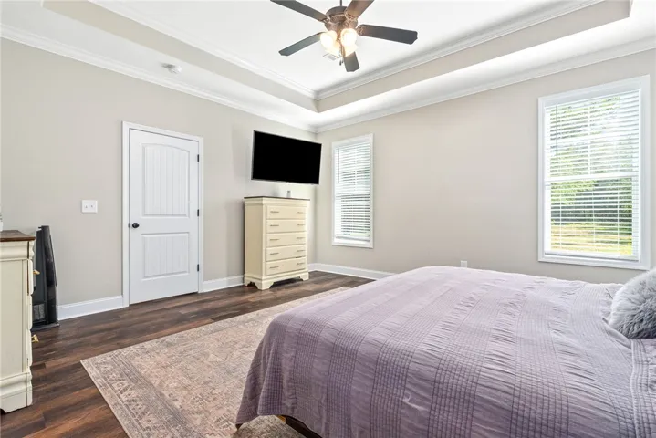 A tray ceiling and large windows illuminate this comfortable bedroom space.