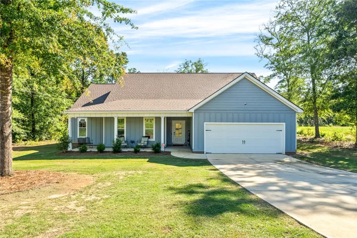 A welcoming front porch invites relaxation in this charming home, set amidst verdant surroundings.