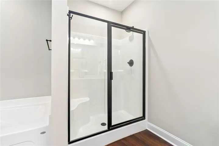 Modern shower enclosure with rich dark hardware complements the deep wood flooring.