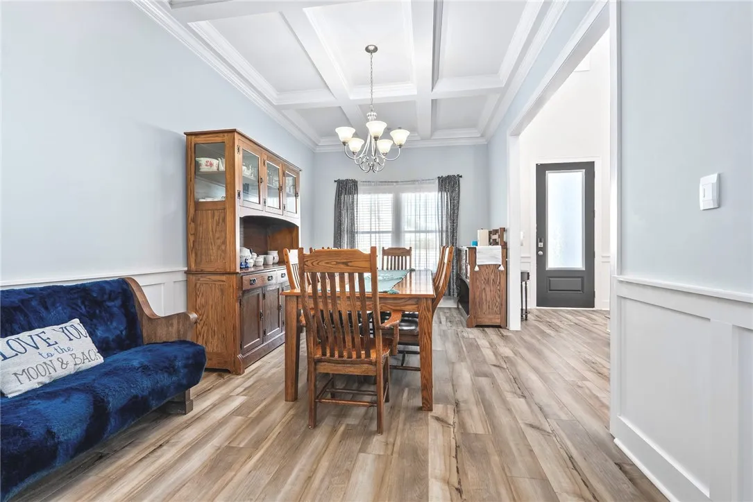 A graceful chandelier illuminates the coffered ceiling above the dining space, highlighting the beautiful wood flooring.