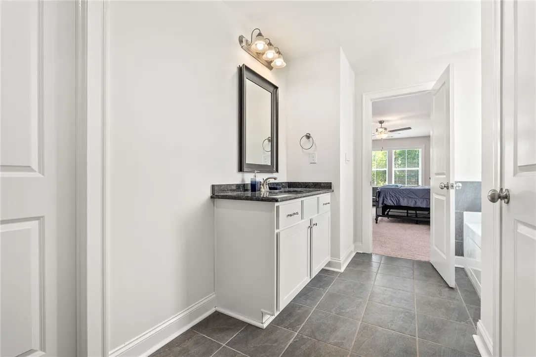 A well-appointed bathroom vanity with granite counters, tile flooring, and a clear view into a sun-filled bedroom.