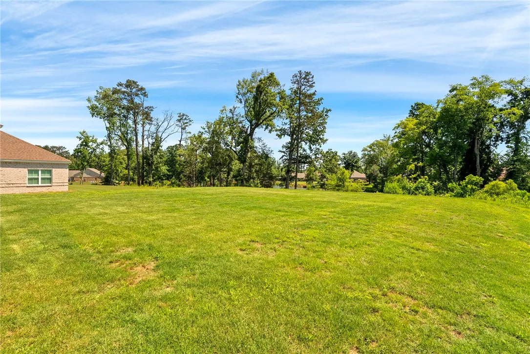 A spacious green lawn extends to a pond, offering abundant natural surroundings and peaceful vistas.
