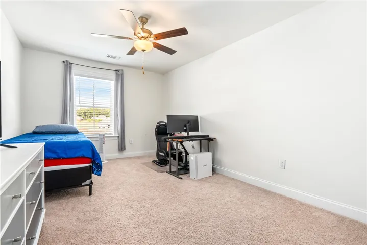A well-lit bedroom features plush carpeting and a modern ceiling fan for ultimate comfort.