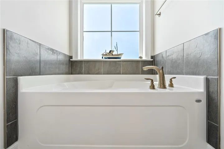 Relax in this inviting tub, featuring sleek hardware and tiled surround.