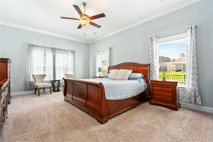 Well-lit primary bedroom featuring crown molding and a prominent ceiling fan.