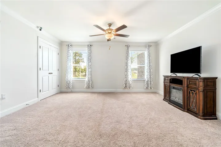 A quiet living area offers soft carpeting, white walls, and a warm ceiling fan light.