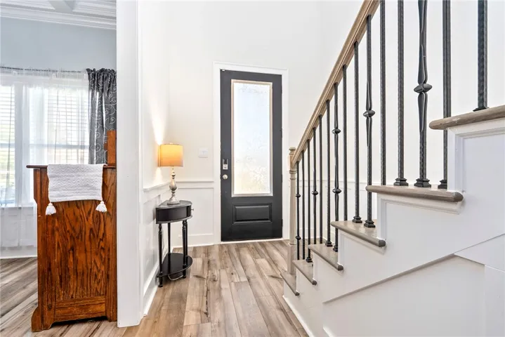 A welcoming entryway with rich wood flooring and a graceful staircase featuring decorative wrought iron balusters.