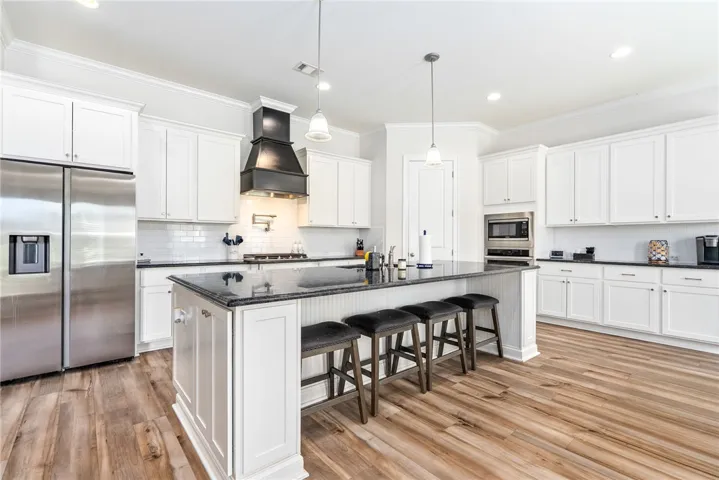 White cabinetry, dark stone countertops, and wood flooring create a modern kitchen with a large island.