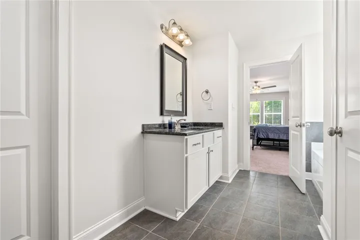 A well-appointed bathroom vanity with granite counters, tile flooring, and a clear view into a sun-filled bedroom.