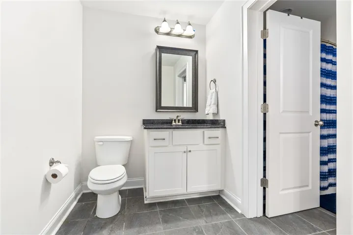 A pristine bathroom features a single vanity, a toilet, and gray tile flooring.