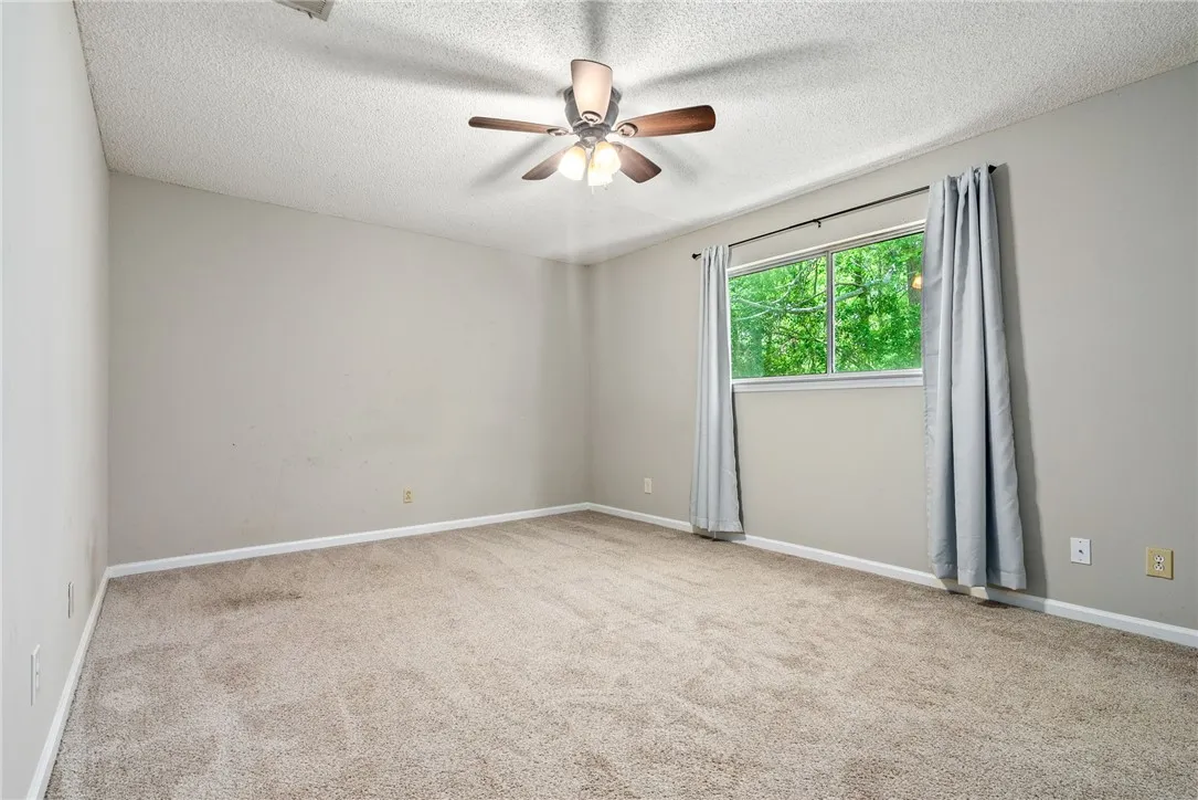 A well-lit bedroom features plush carpeting and a verdant outdoor outlook.