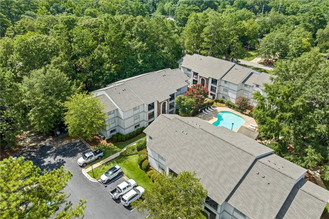 An aerial perspective reveals a well-maintained apartment complex nestled amidst lush green trees, featuring a sparkling community pool.