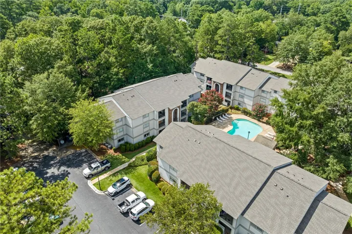 An aerial perspective reveals a well-maintained apartment complex nestled amidst lush green trees, featuring a sparkling community pool.