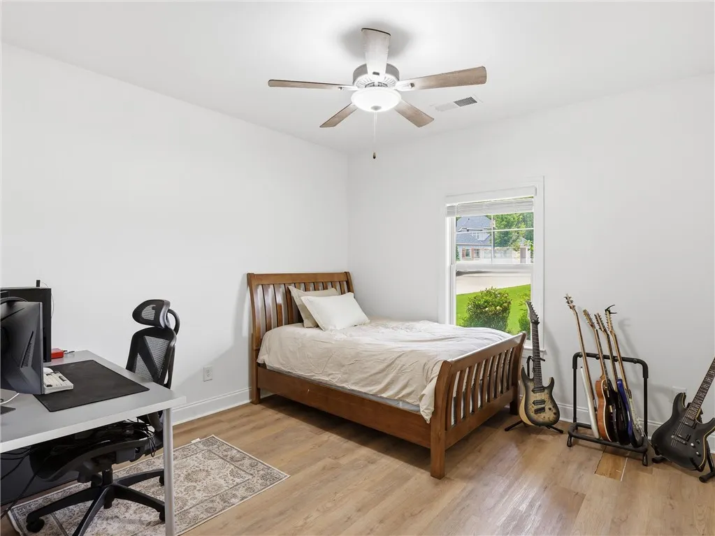 A well-lit bedroom featuring durable hardwood flooring and a functional ceiling fan for comfort.