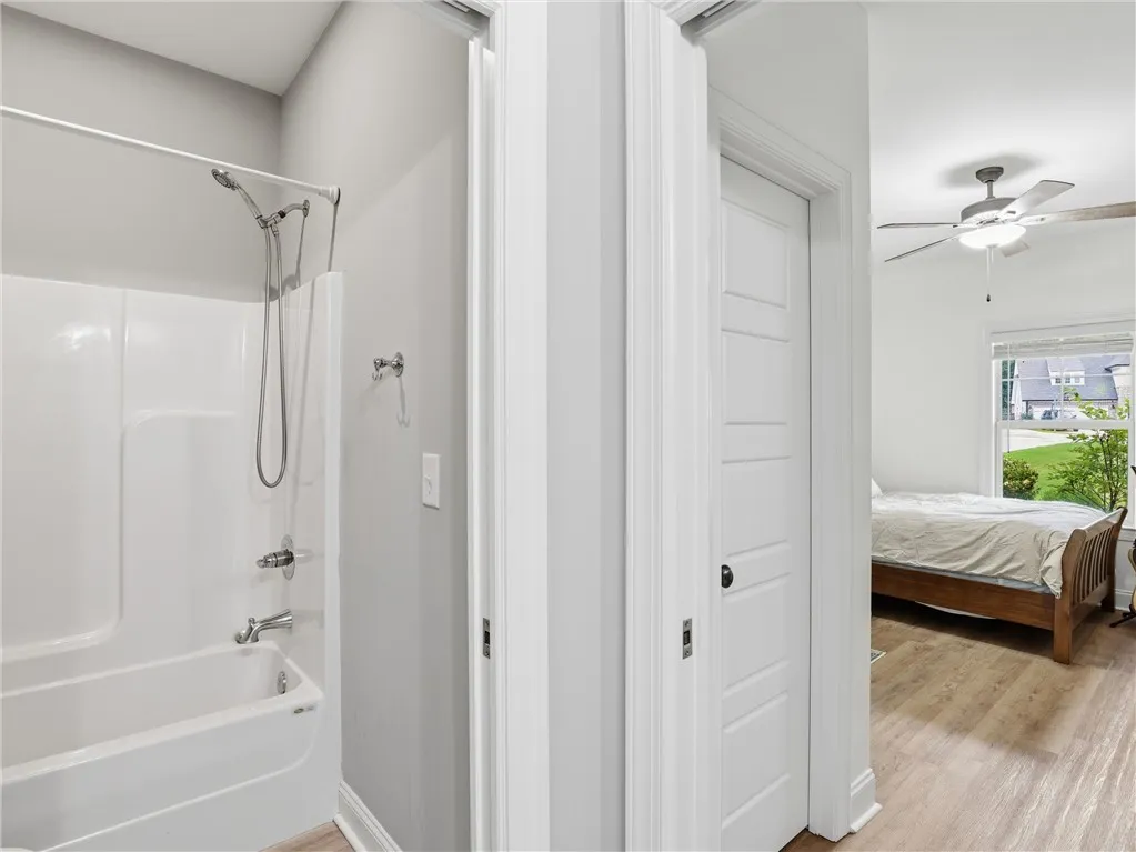 Functional bath with integrated shower and tub serves an adjoining bedroom featuring a ceiling fan.