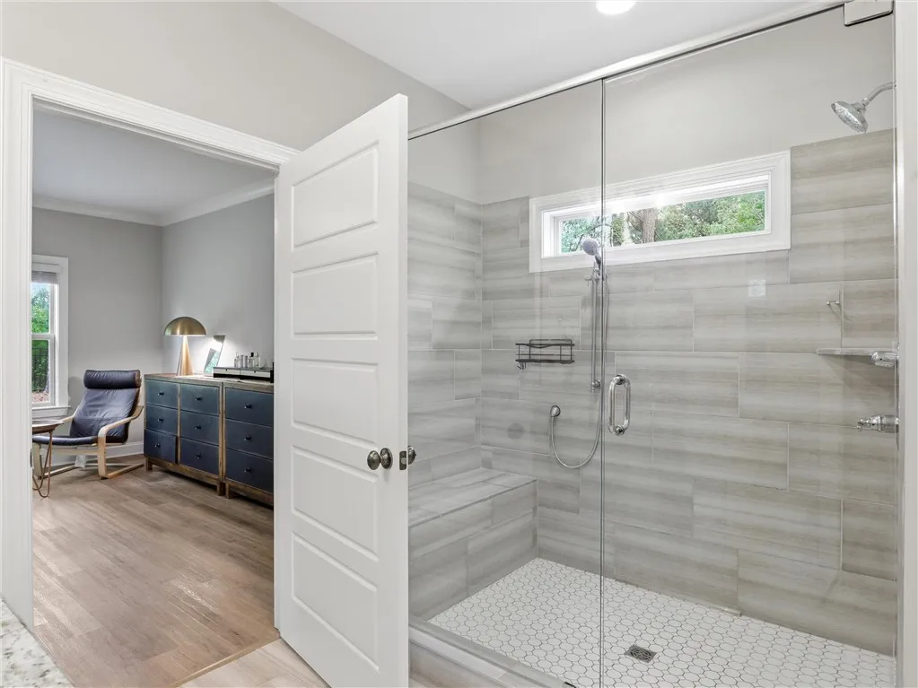 A sleek, tiled walk-in shower with a glass enclosure connects to a brightly lit room.