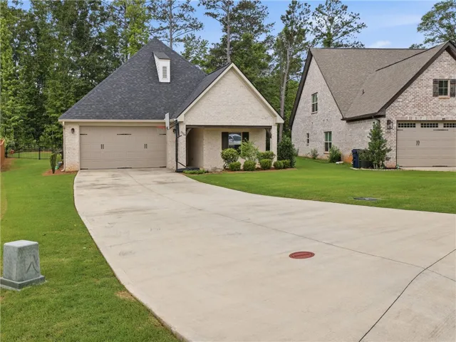 A graceful concrete driveway leads to this charming residence, framed by vibrant green lawns and mature trees.