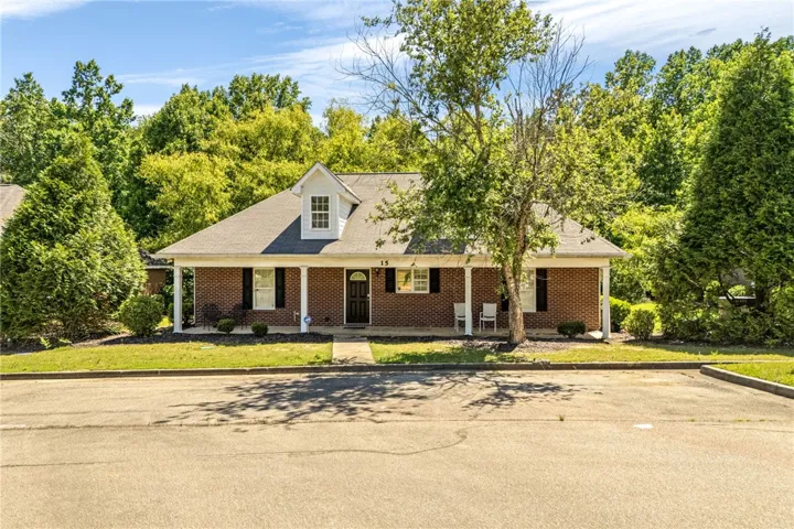 A charming brick residence awaits, nestled amidst a lush, verdant backdrop, featuring a welcoming covered porch.