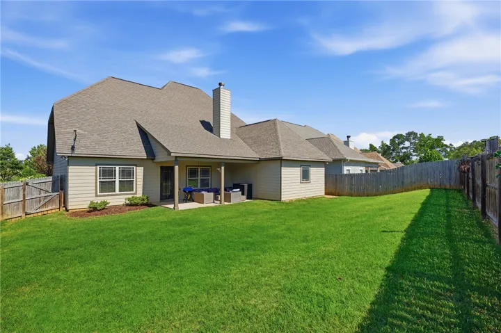 A spacious backyard with vibrant green grass, offering a private covered patio for relaxation.