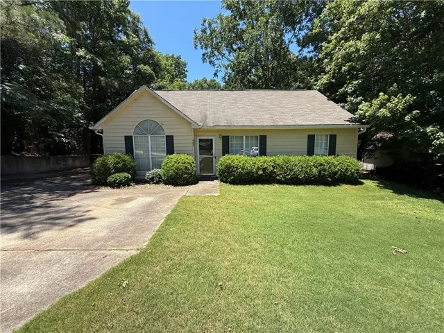 A classic ranch home features a verdant lawn and a mature tree-lined backdrop.